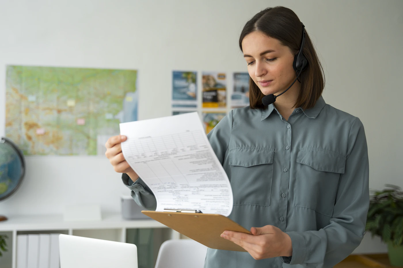 A professional woman wearing a headset reading a document on a clipboard at a calm office desk