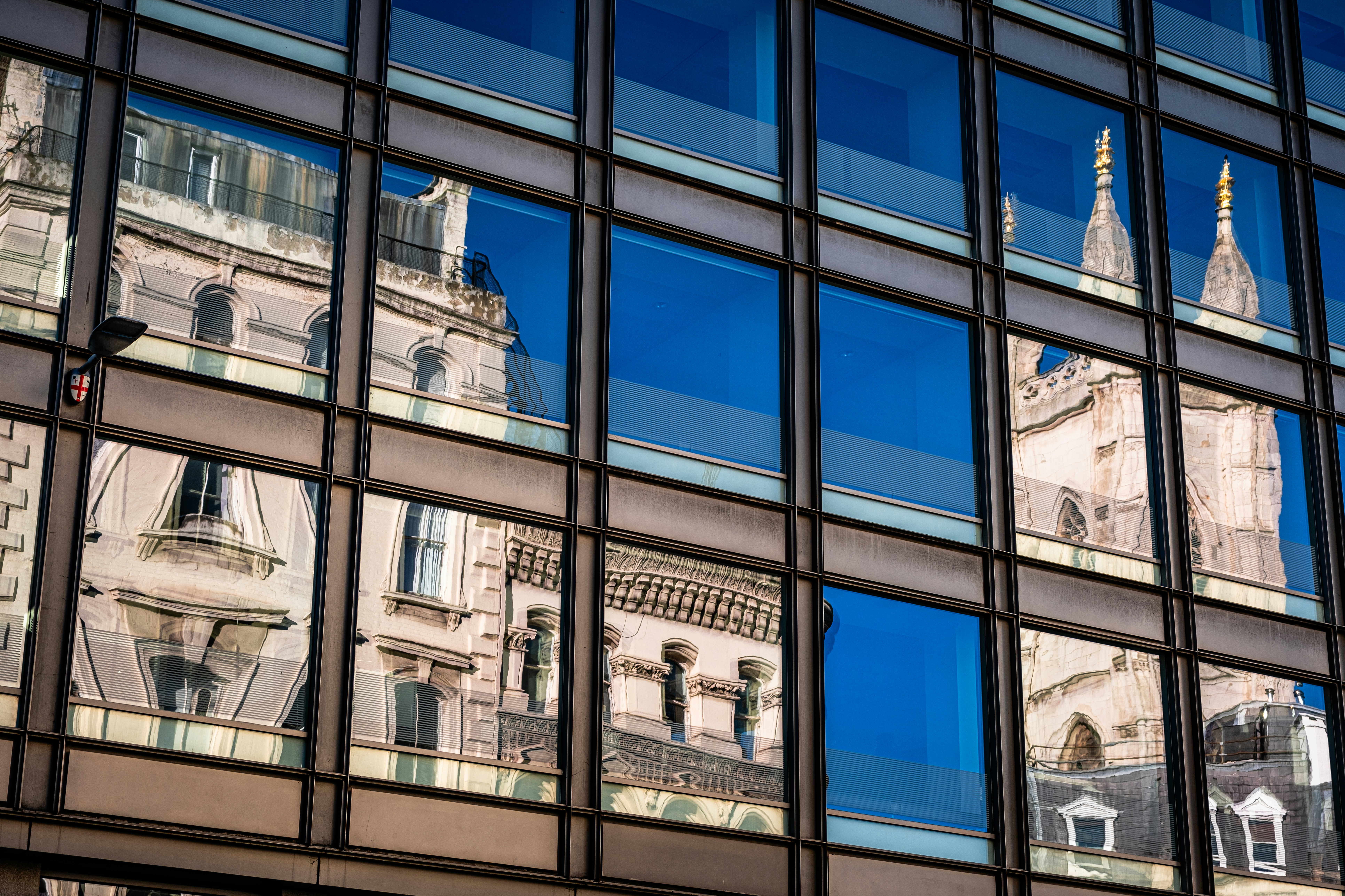 The windows of modern, mirrored office building reflect the historic buildings around it