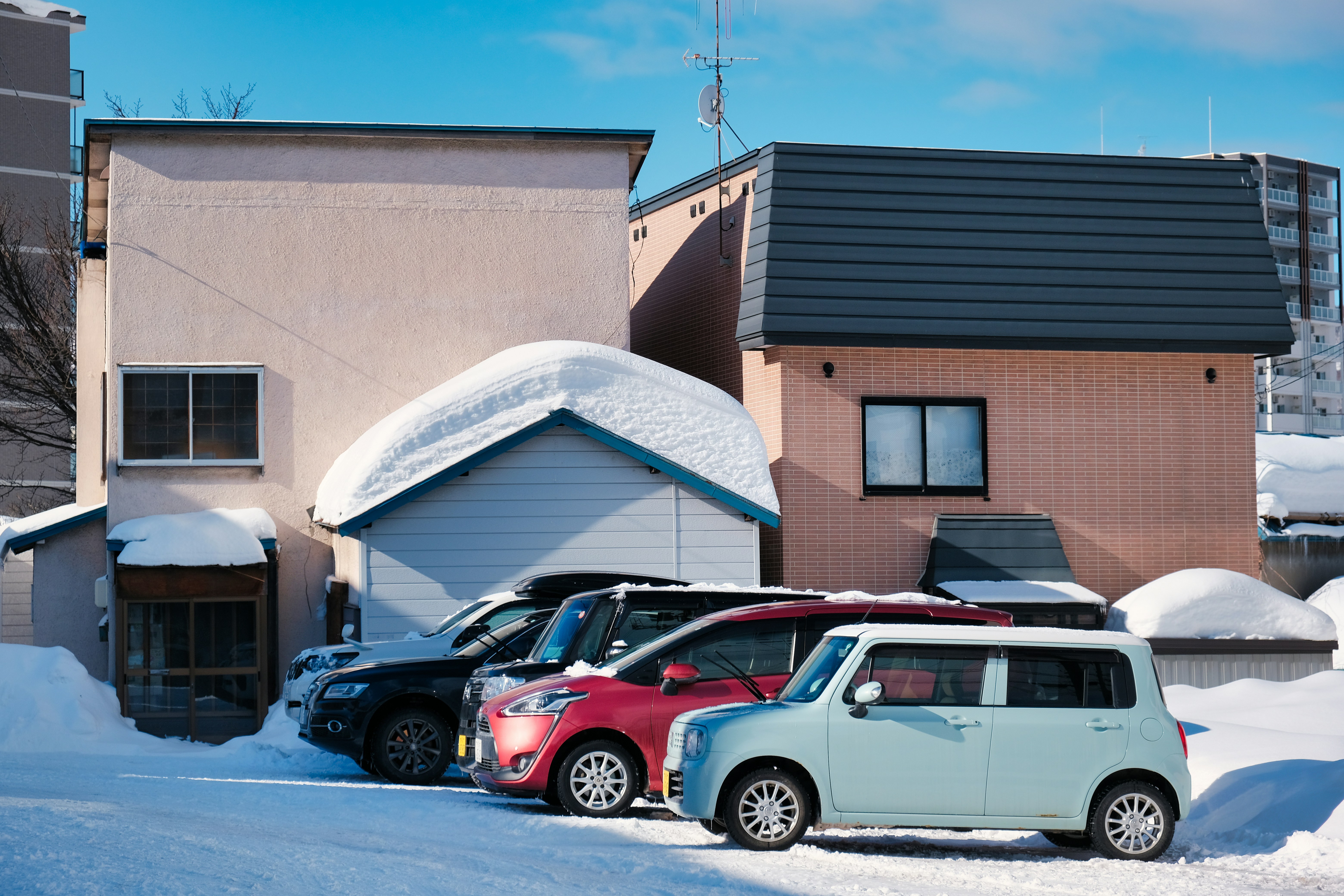 A row of cars parked in front of a house covered in snow