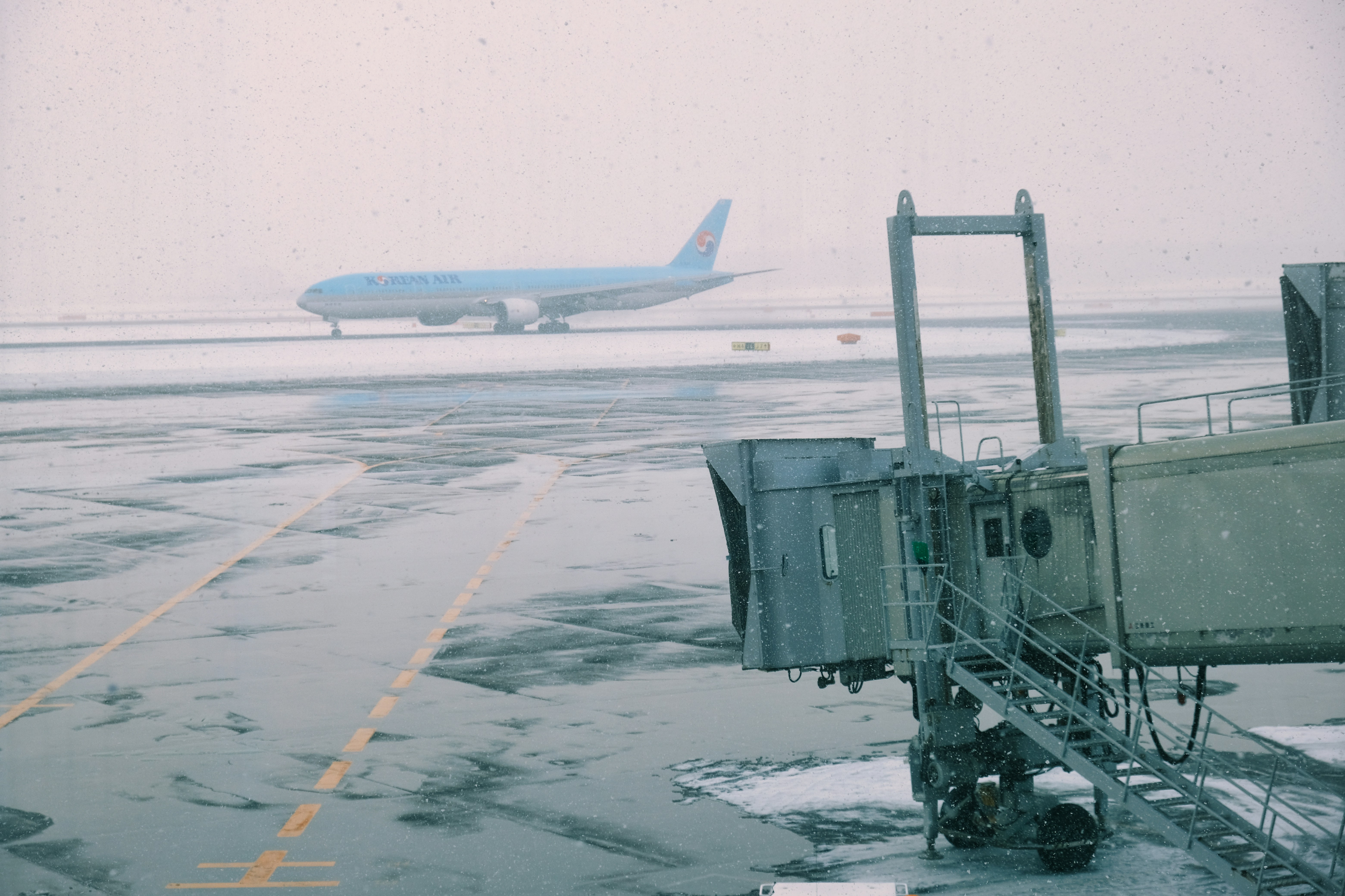 Snow removal equipment clearing runway at Japanese airport, airplane being de-iced