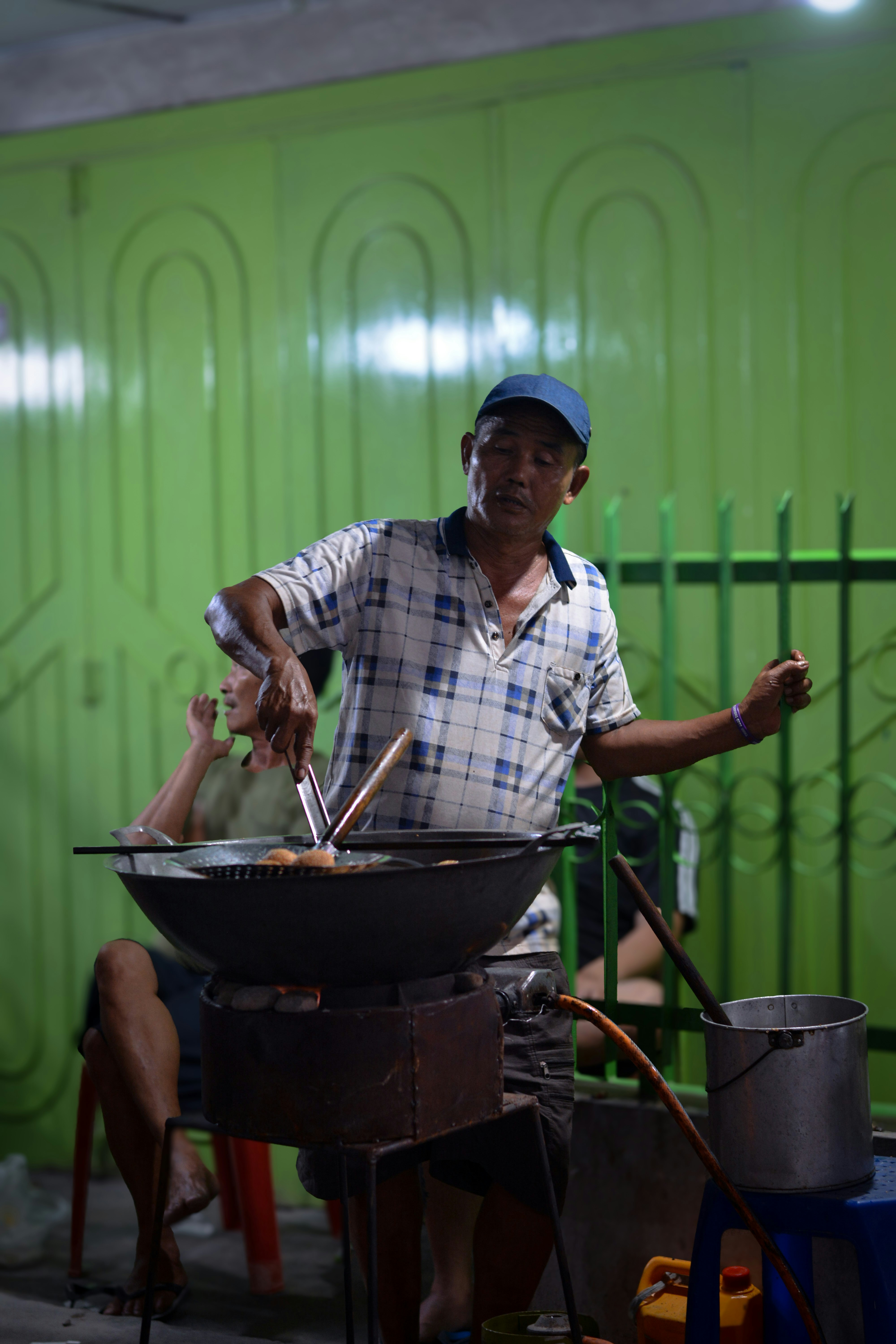 A man cooking food on a grill in front of a green wall