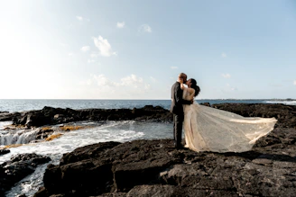 A bride and groom standing on a rocky beach