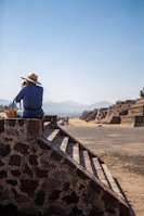A man in a hat sitting on top of a stone structure