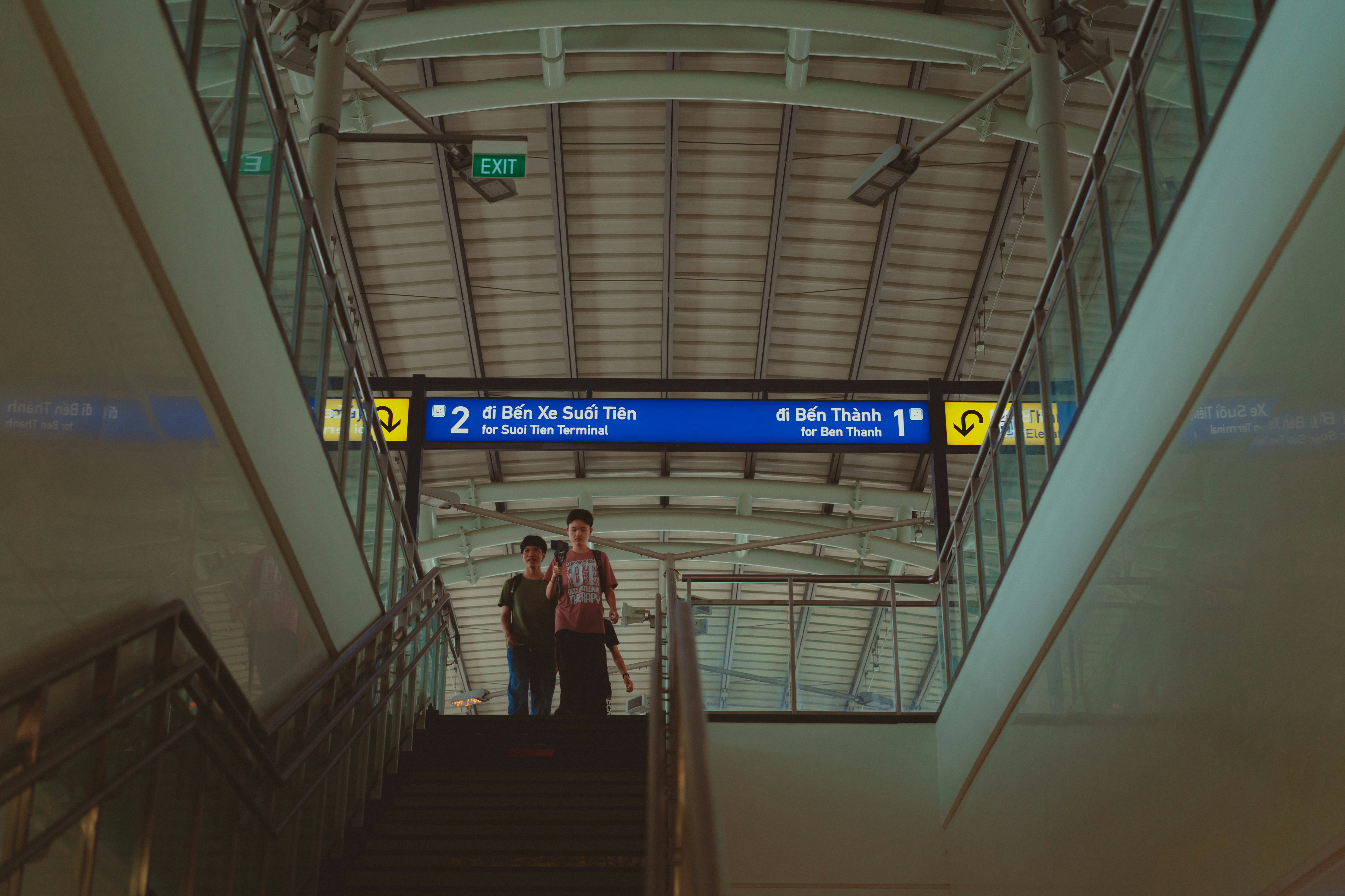 A couple of people that are walking down some stairs, wondering around metro station in saigon