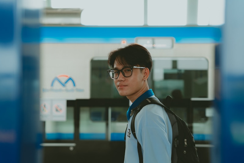 A man with glasses and a backpack standing in front of a train