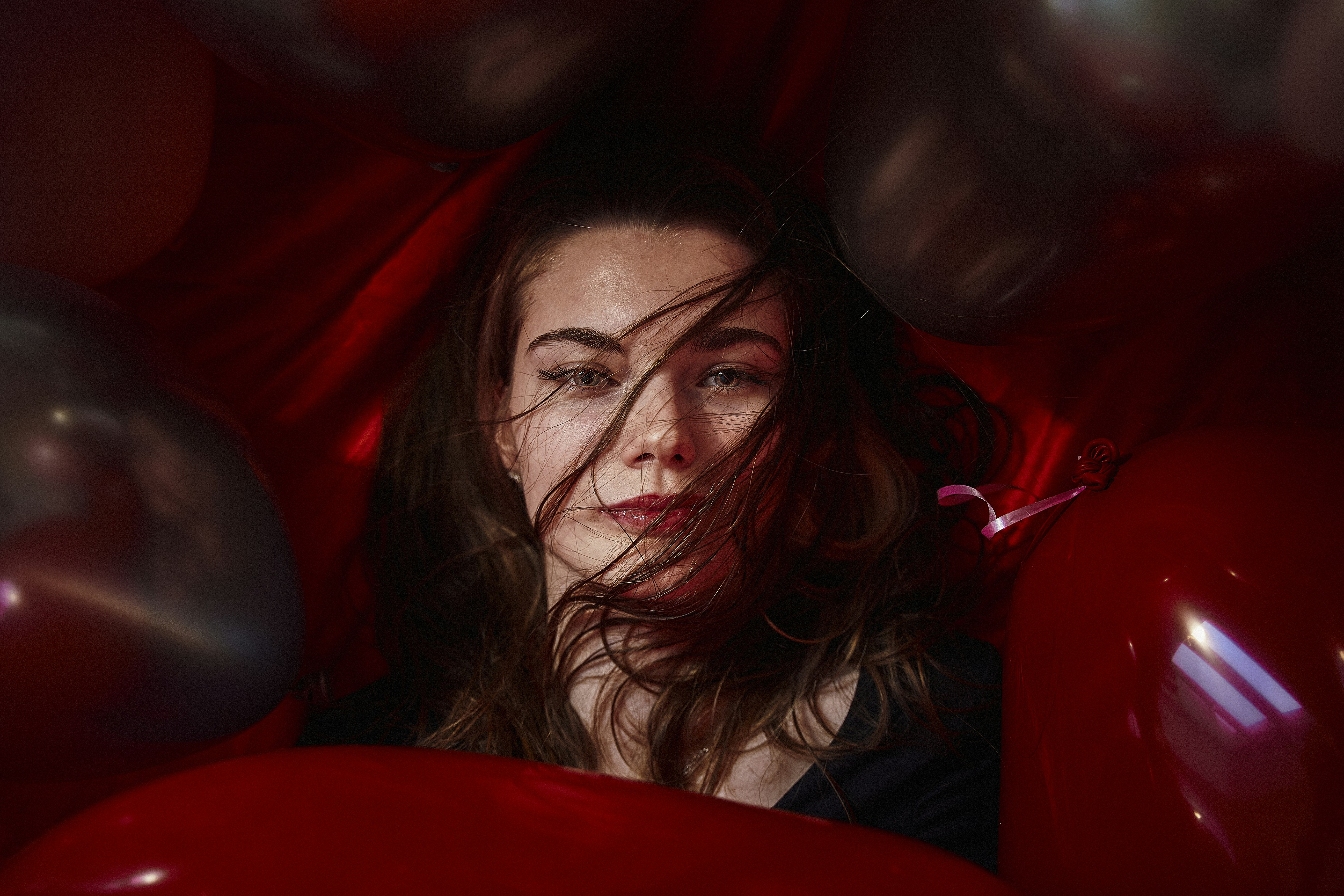 A woman is surrounded by red balloons