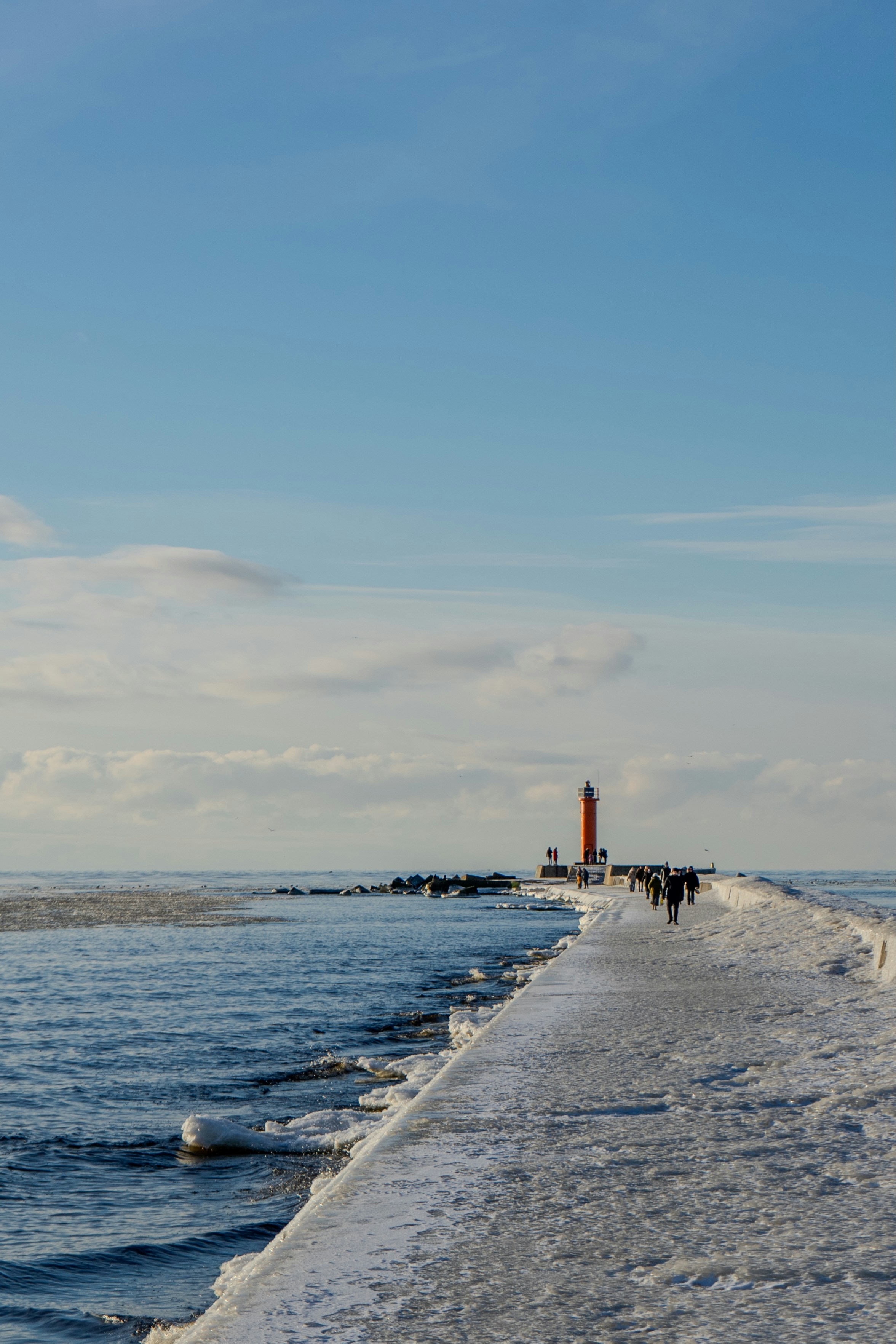 People walking along a snow covered pier next to the ocean