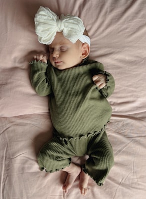 A baby sleeping on a bed wearing a green outfit