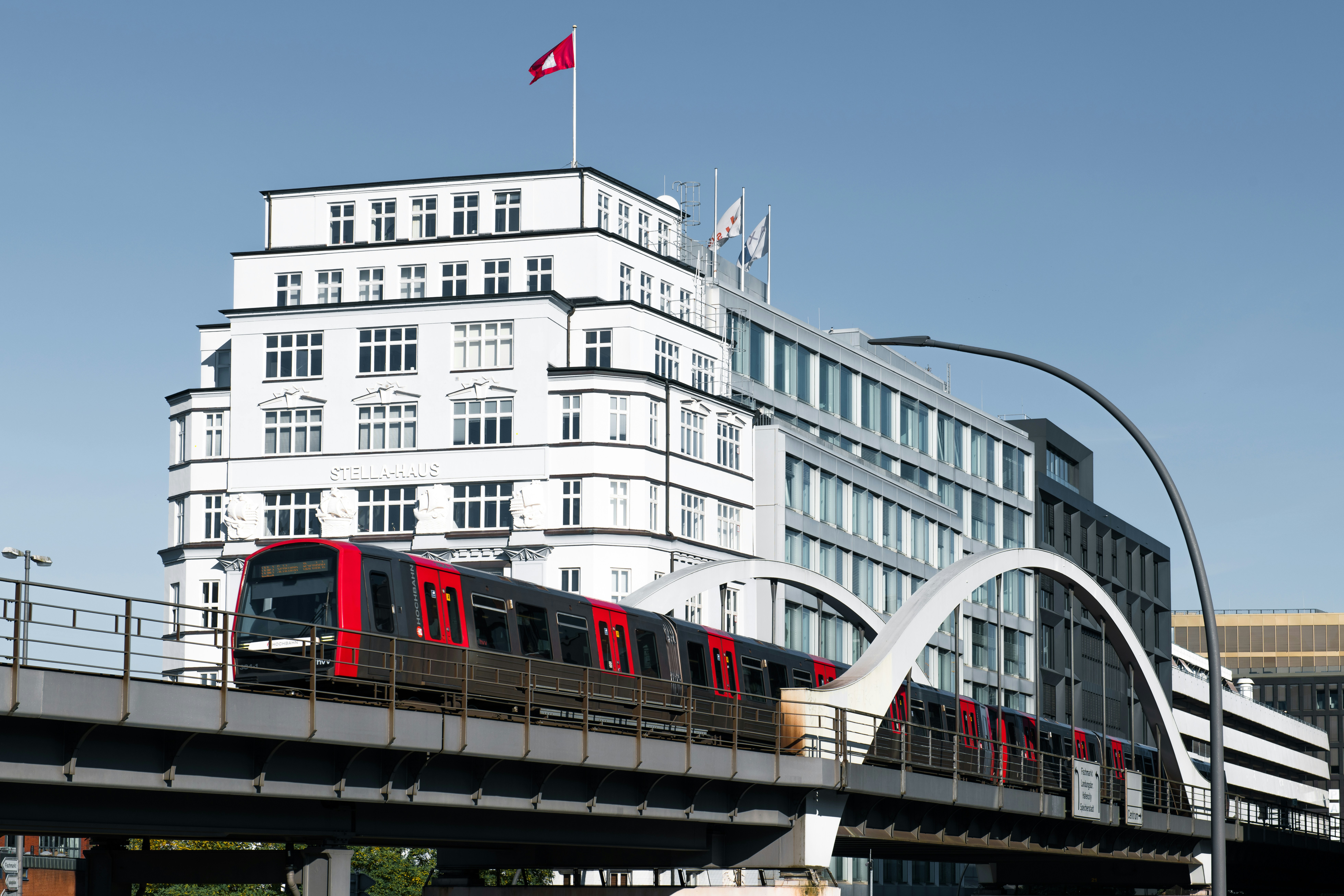 A red train traveling over a bridge next to tall buildings