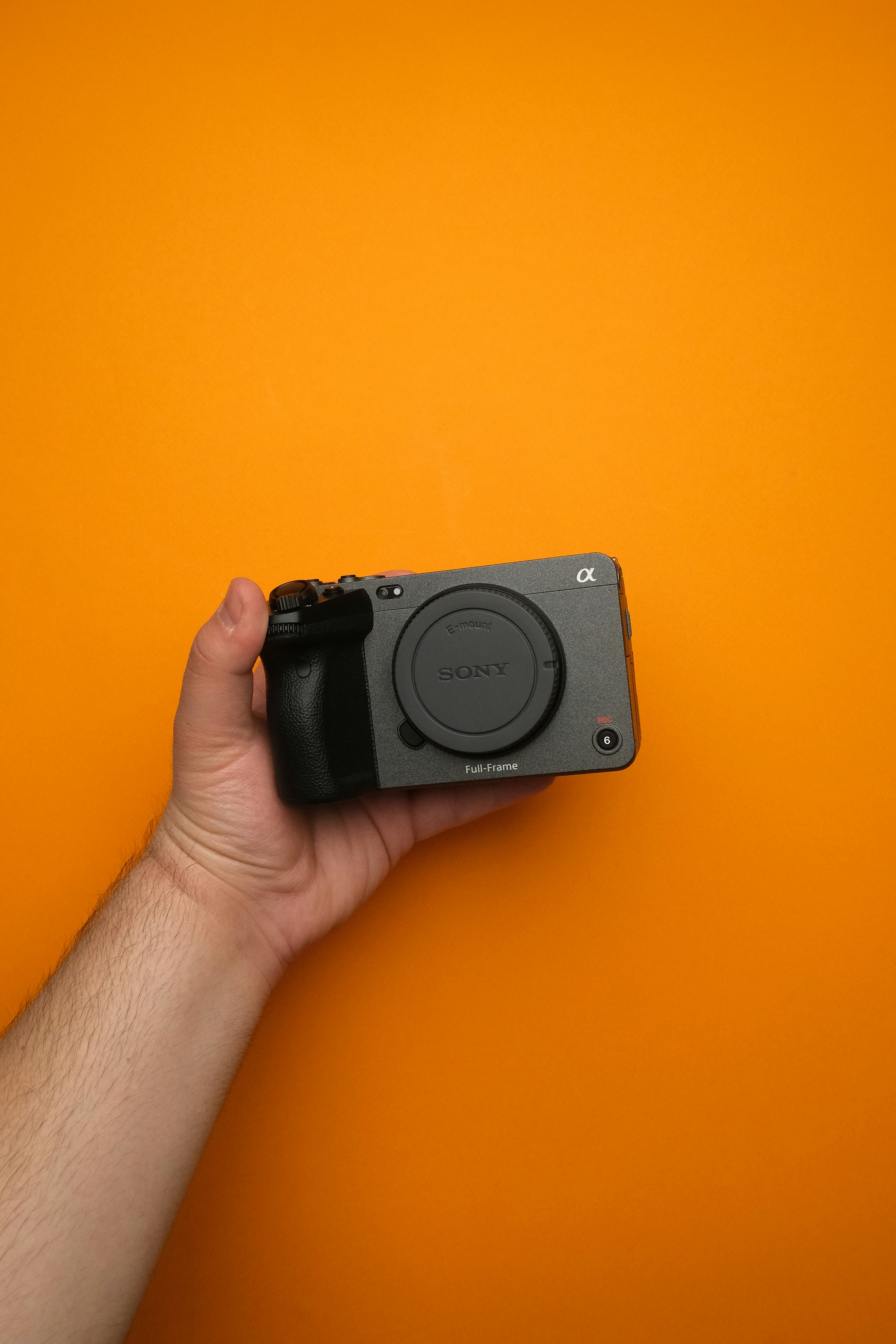 A hand holding a camera on an orange background