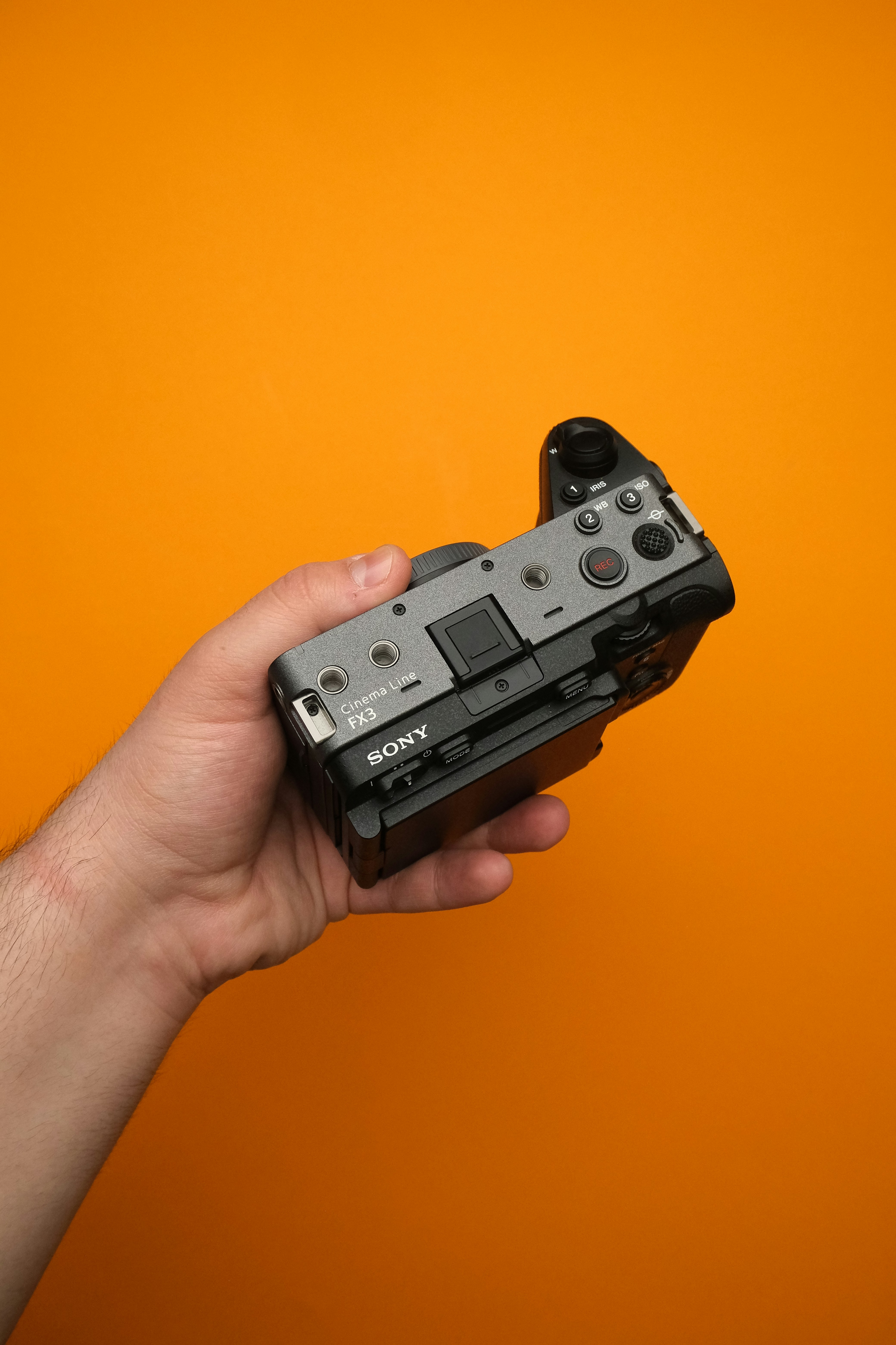 A hand holding a camera on an orange background