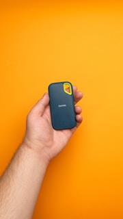 A hand holding a cell phone against a yellow background