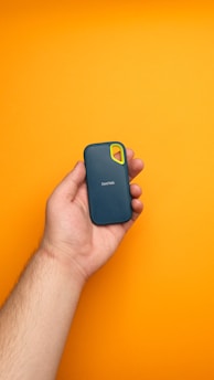 A hand holding a cell phone against a yellow background