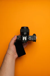 A hand holding a camera on a yellow background