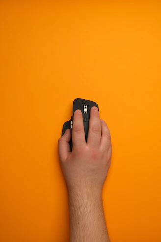 A hand holding a remote control on an orange background