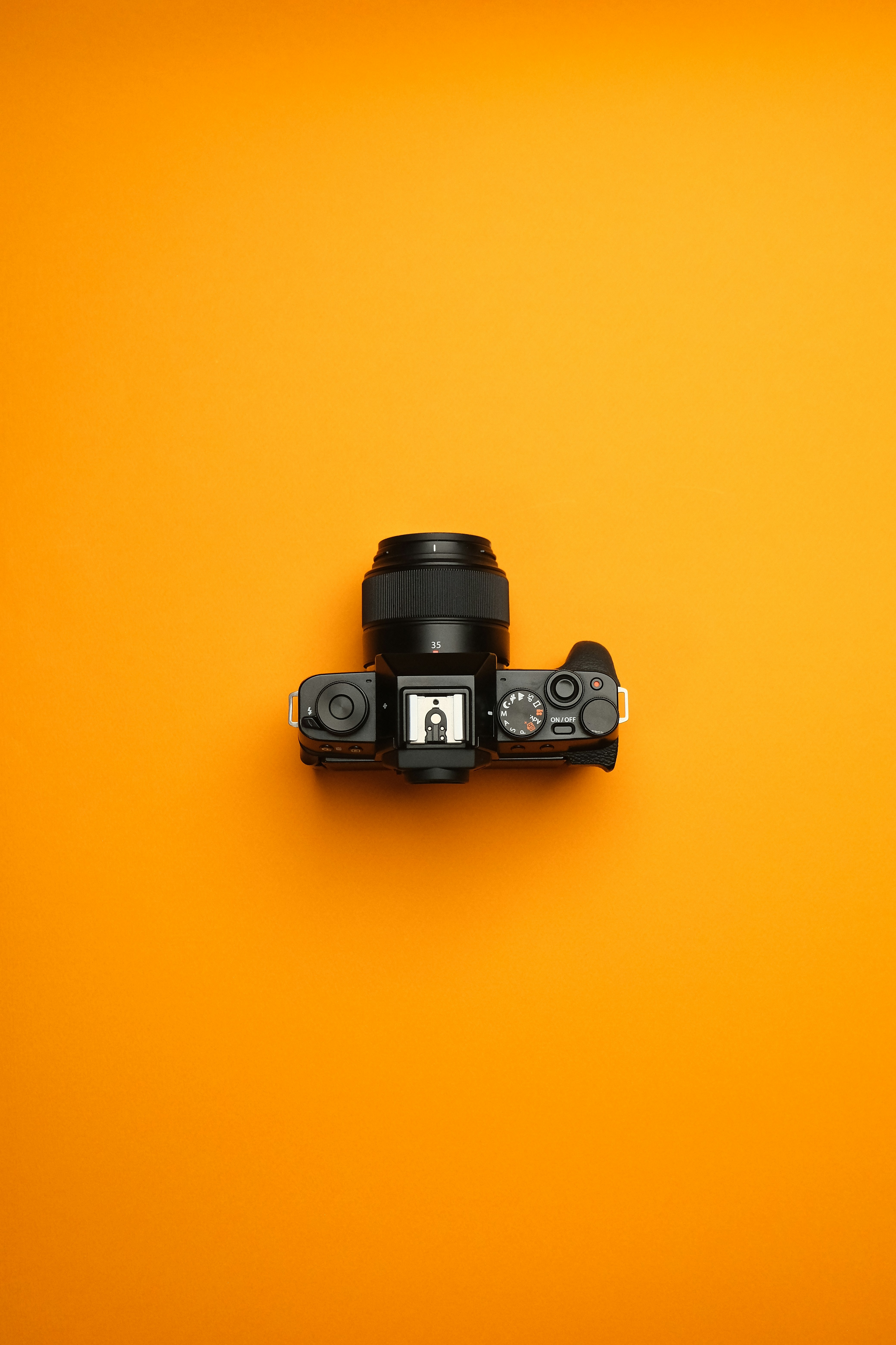 A camera on a yellow background with a black lens