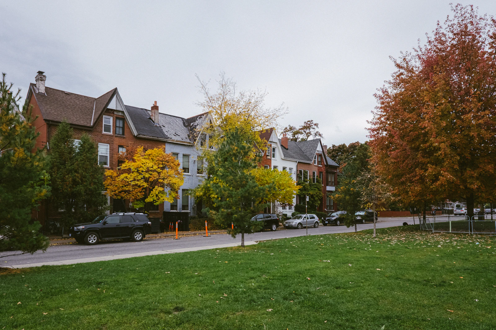 Tree-lined Toronto residential street with brick homes beside a small park in autumn