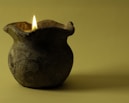 A clay vase with a lit candle in it