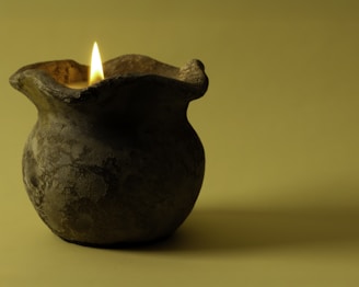 A clay vase with a lit candle in it