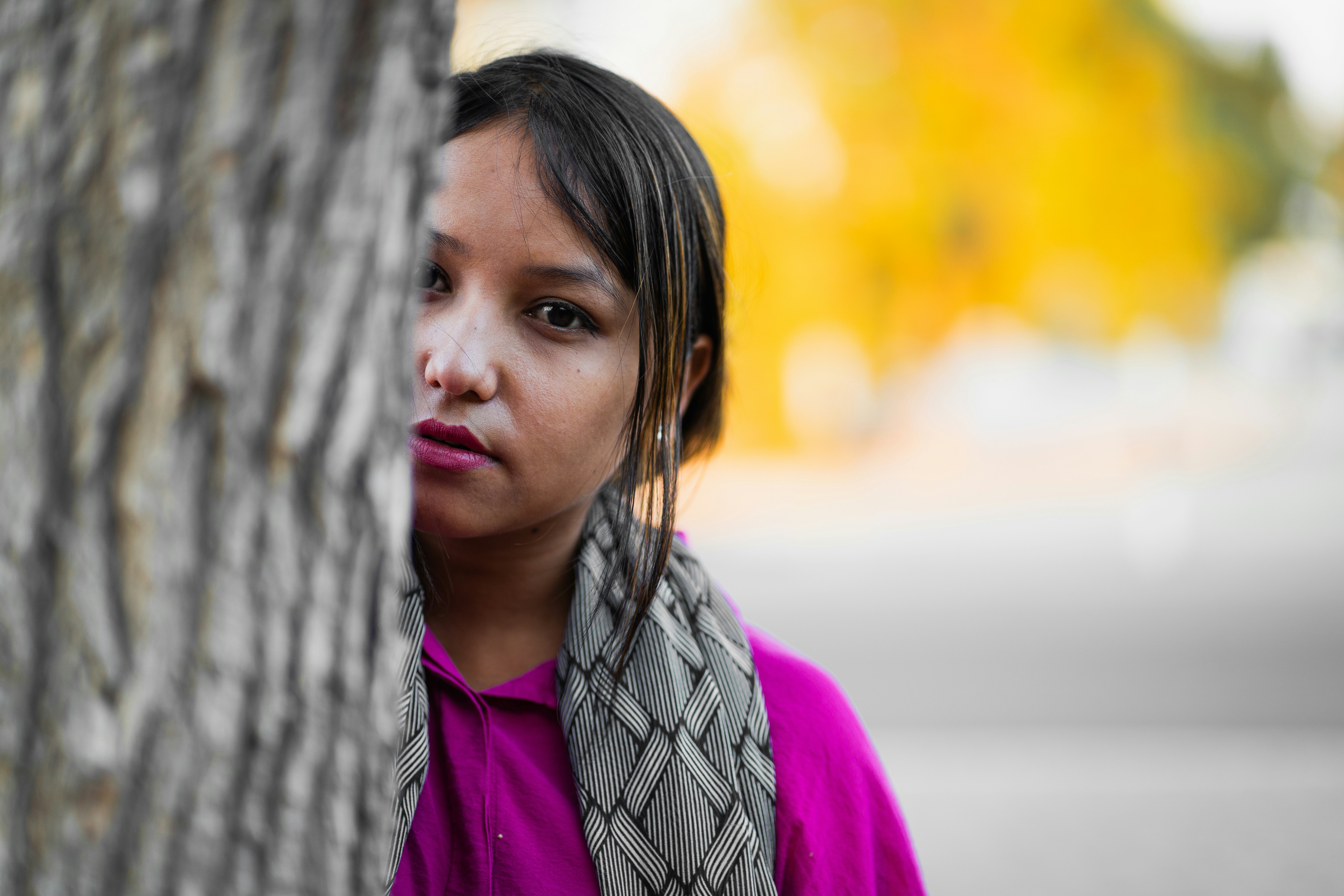 A woman standing next to a tree with a scarf around her neck