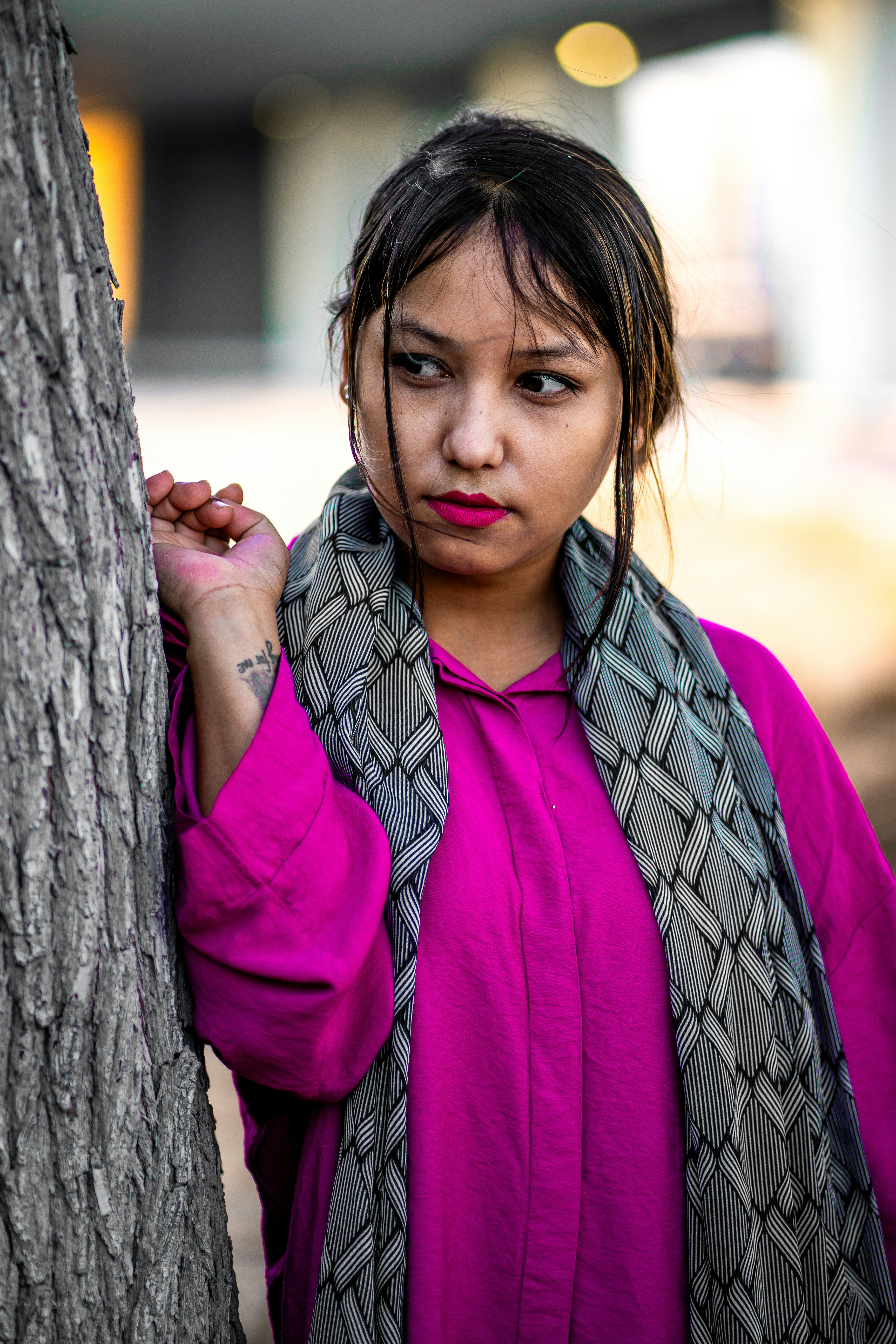 A woman leaning against a tree wearing a scarf