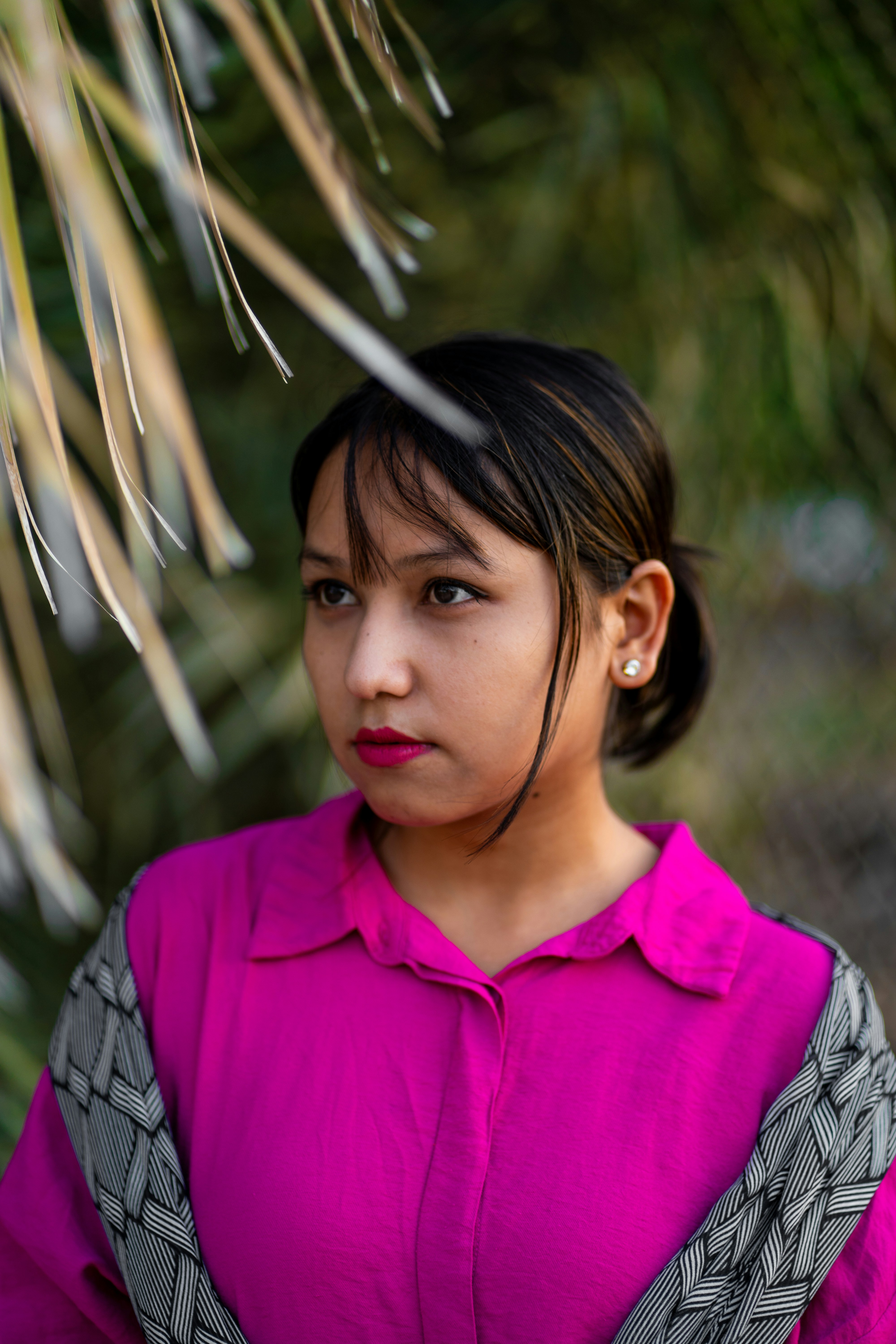 A woman in a pink shirt is standing under a palm tree