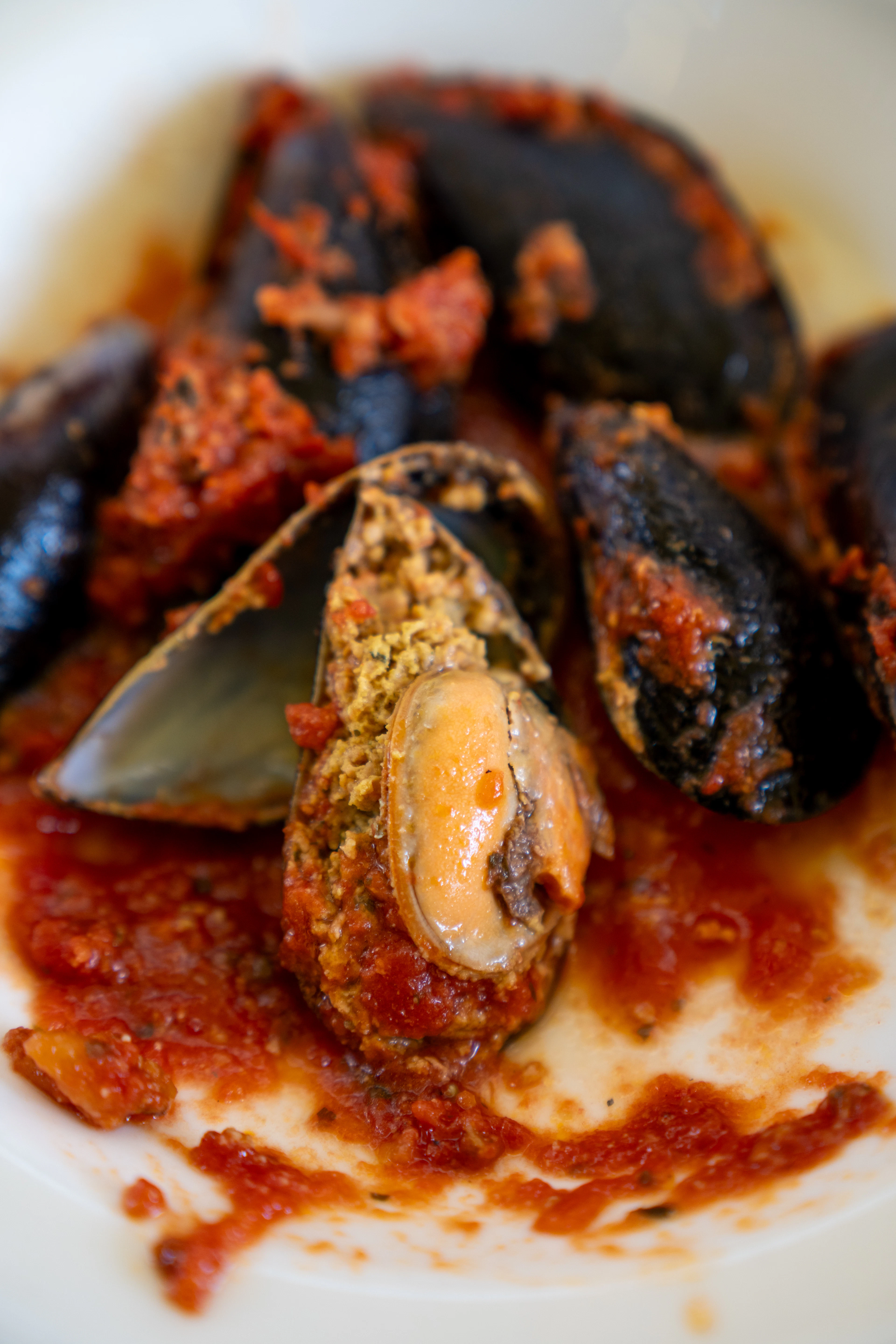 Mussels na buzaru in a shallow white bowl, opened shells sitting in a coarse tomato, garlic and parsley sauce