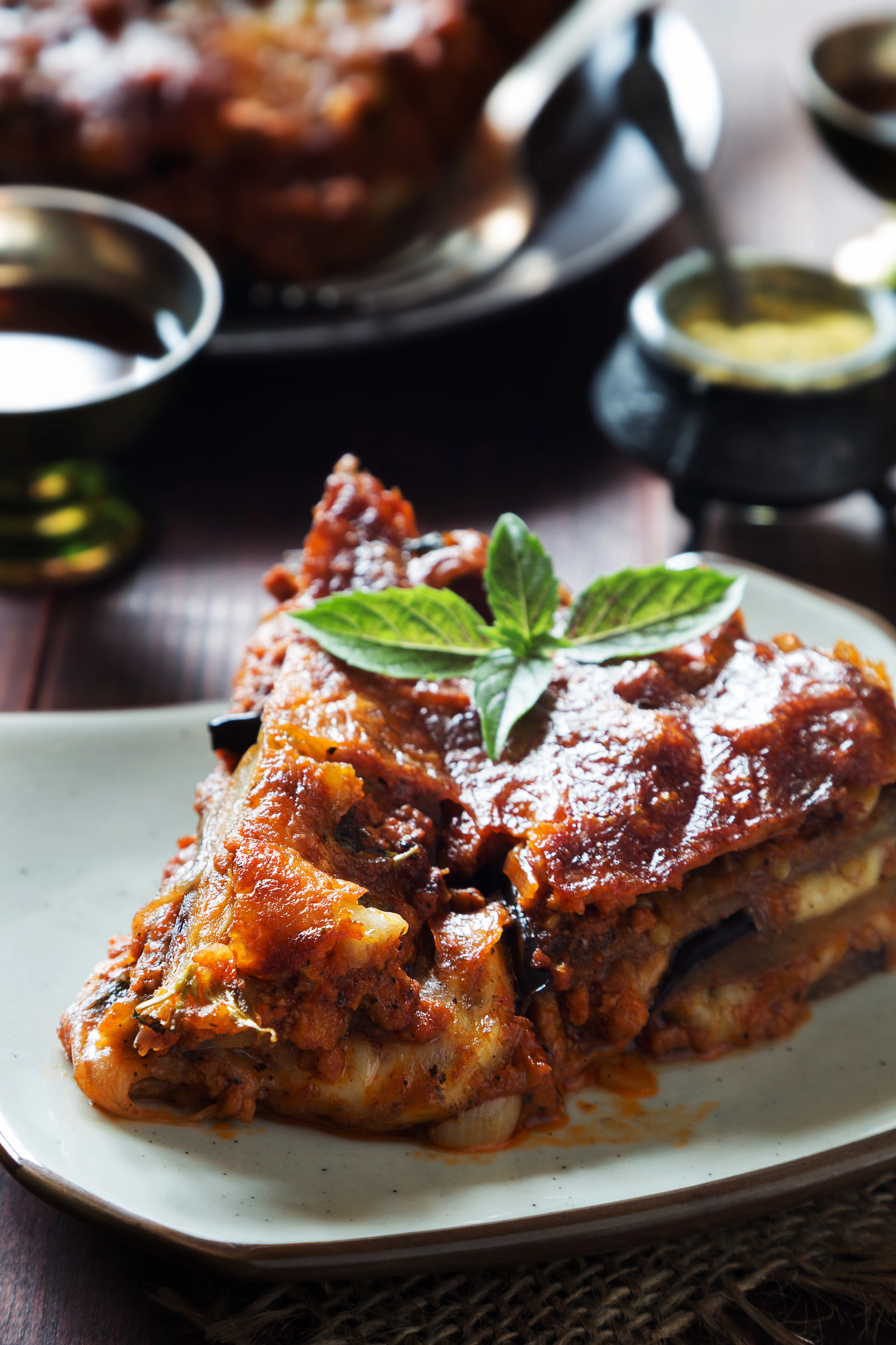 A square of baked lasagna under basil on a white plate