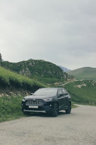 A black car driving down a road next to a lush green hillside