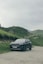 A black car driving down a road next to a lush green hillside