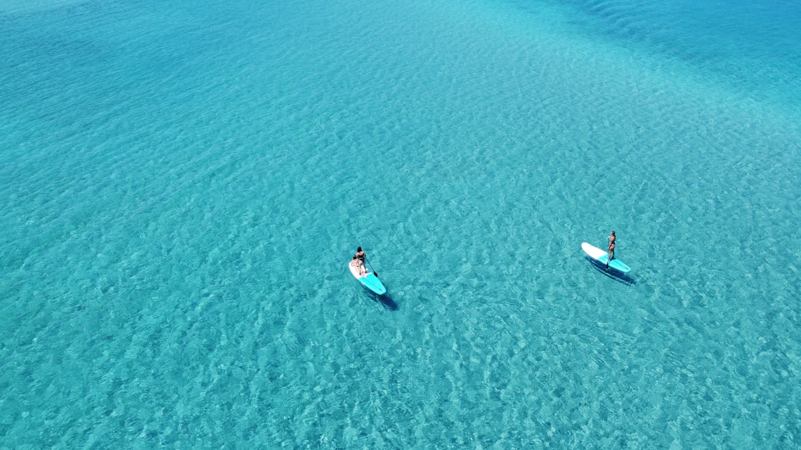 Two paddleboarders gliding across clear turquoise coastal water