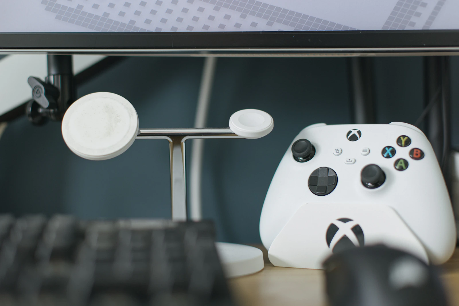 White gaming controller beside a keyboard and charging stand