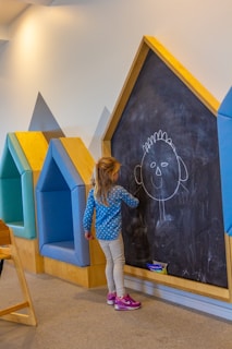 A little girl writing on a blackboard in a room