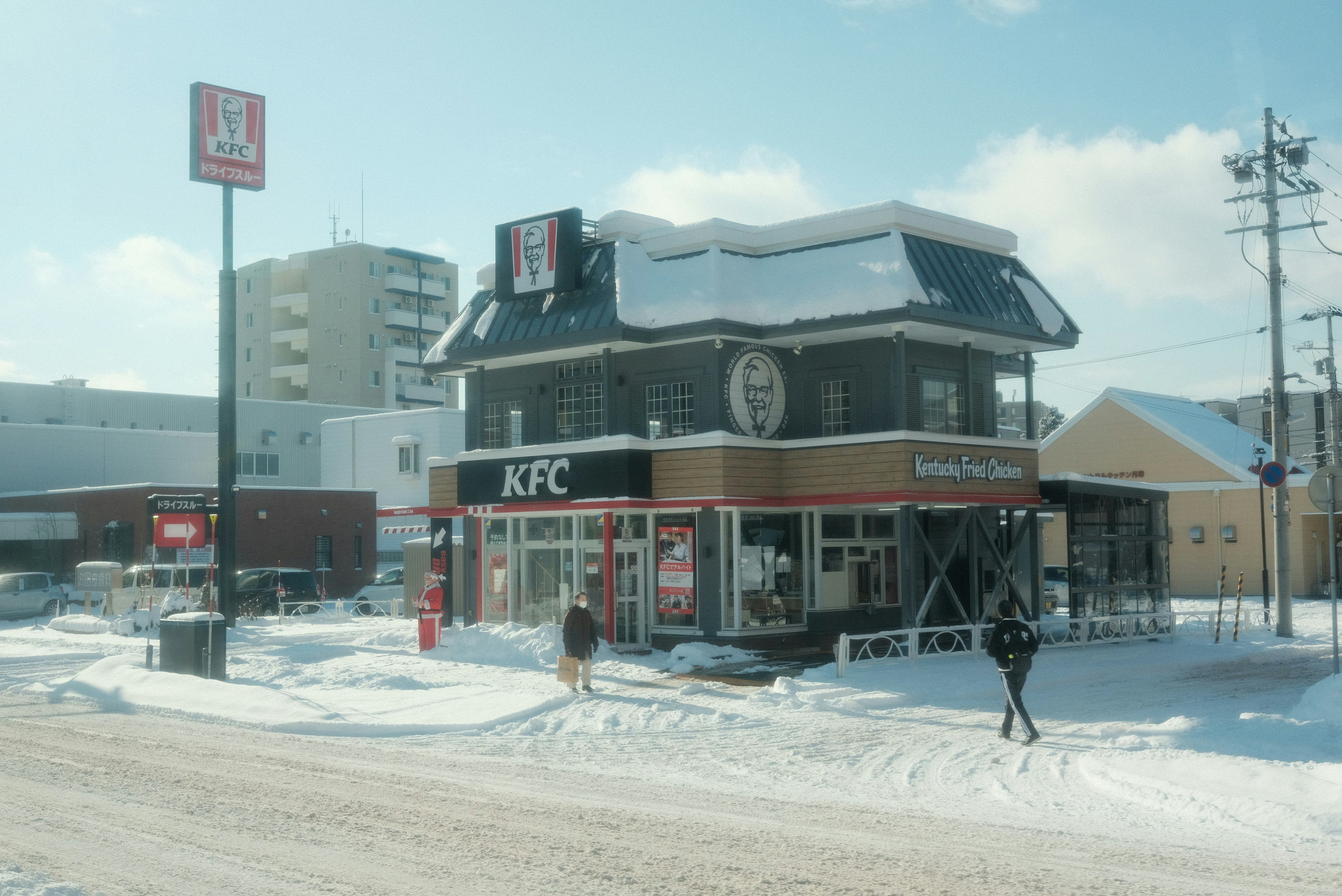 A person walking in the snow in front of a building
