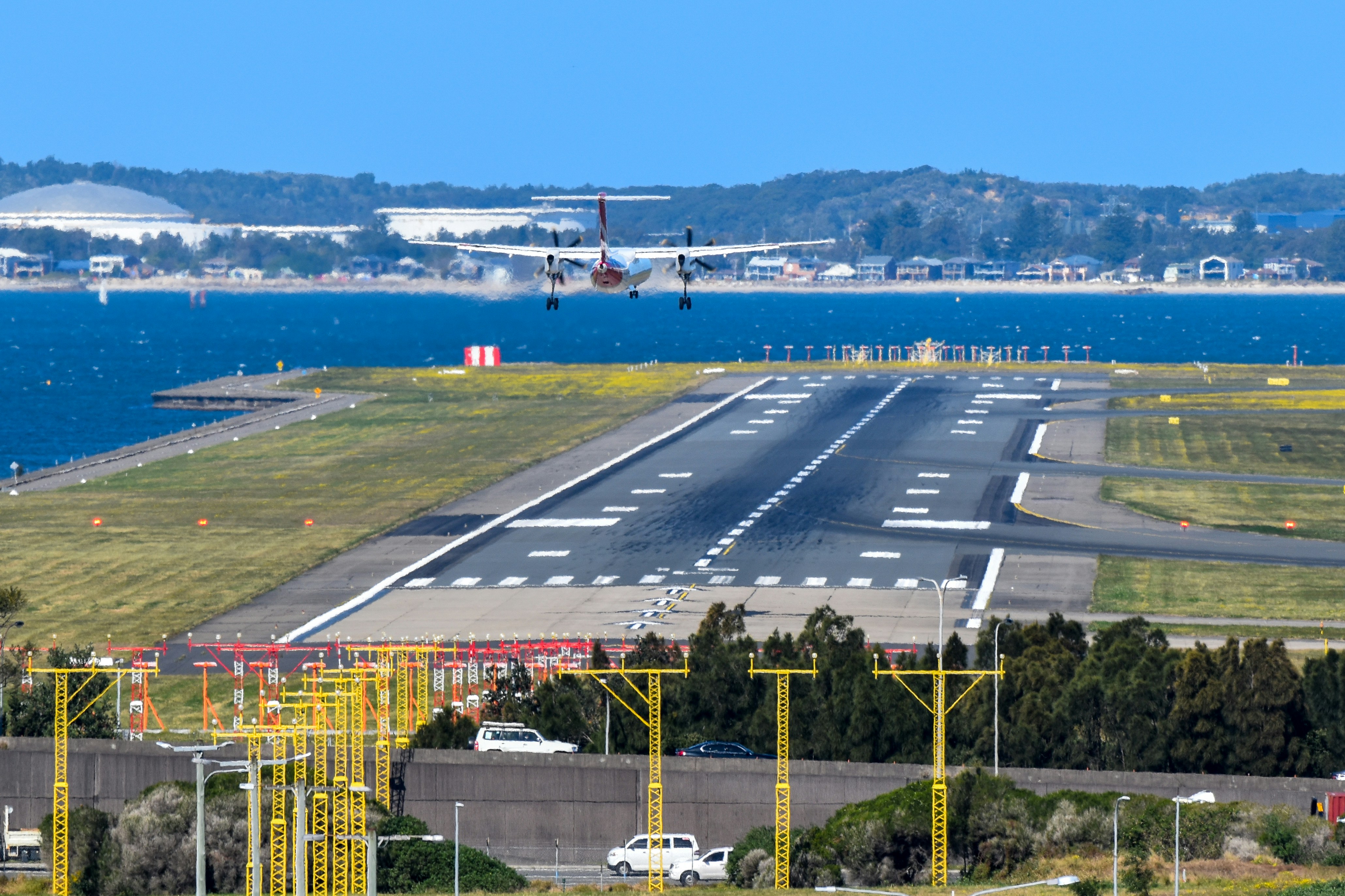 An airport runway with a plane on the runway, QantasLink Q400 landing at Sydney Airport