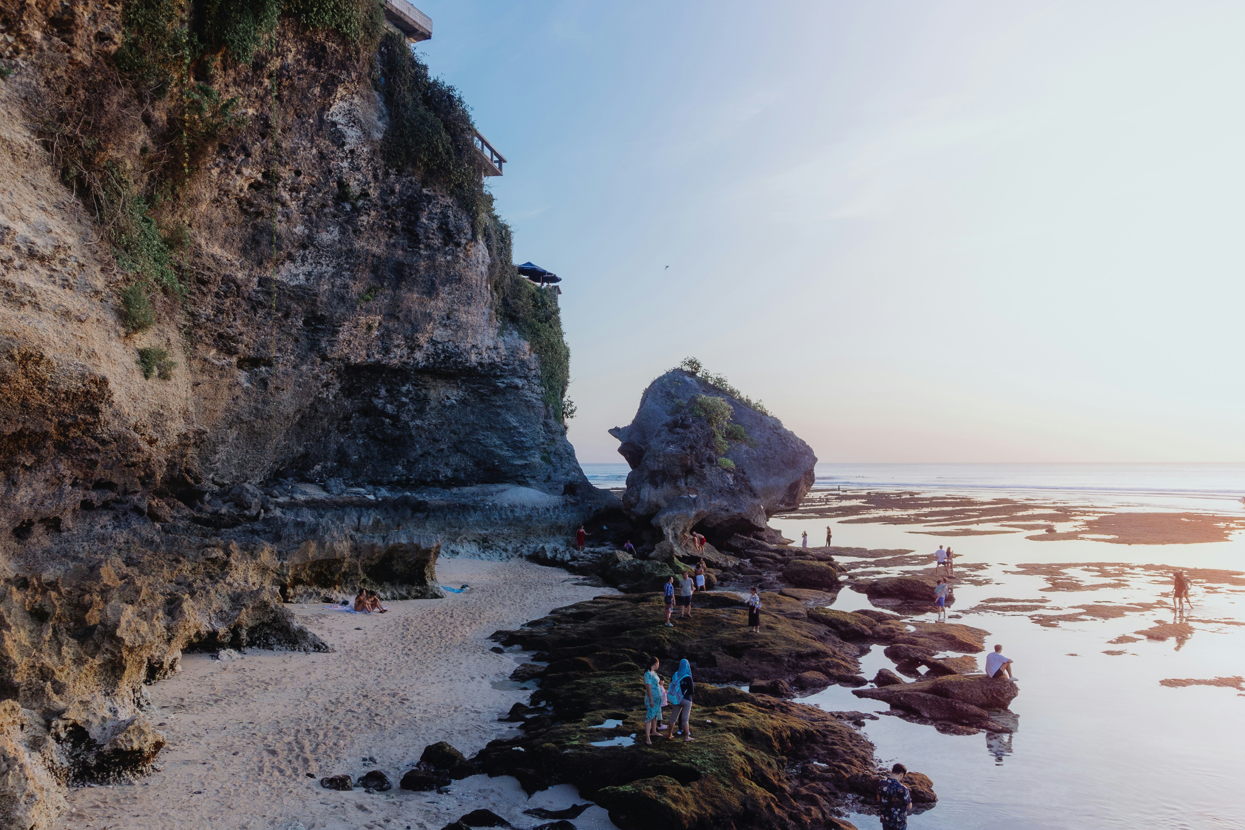 A group of people standing on top of a beach next to a cliff