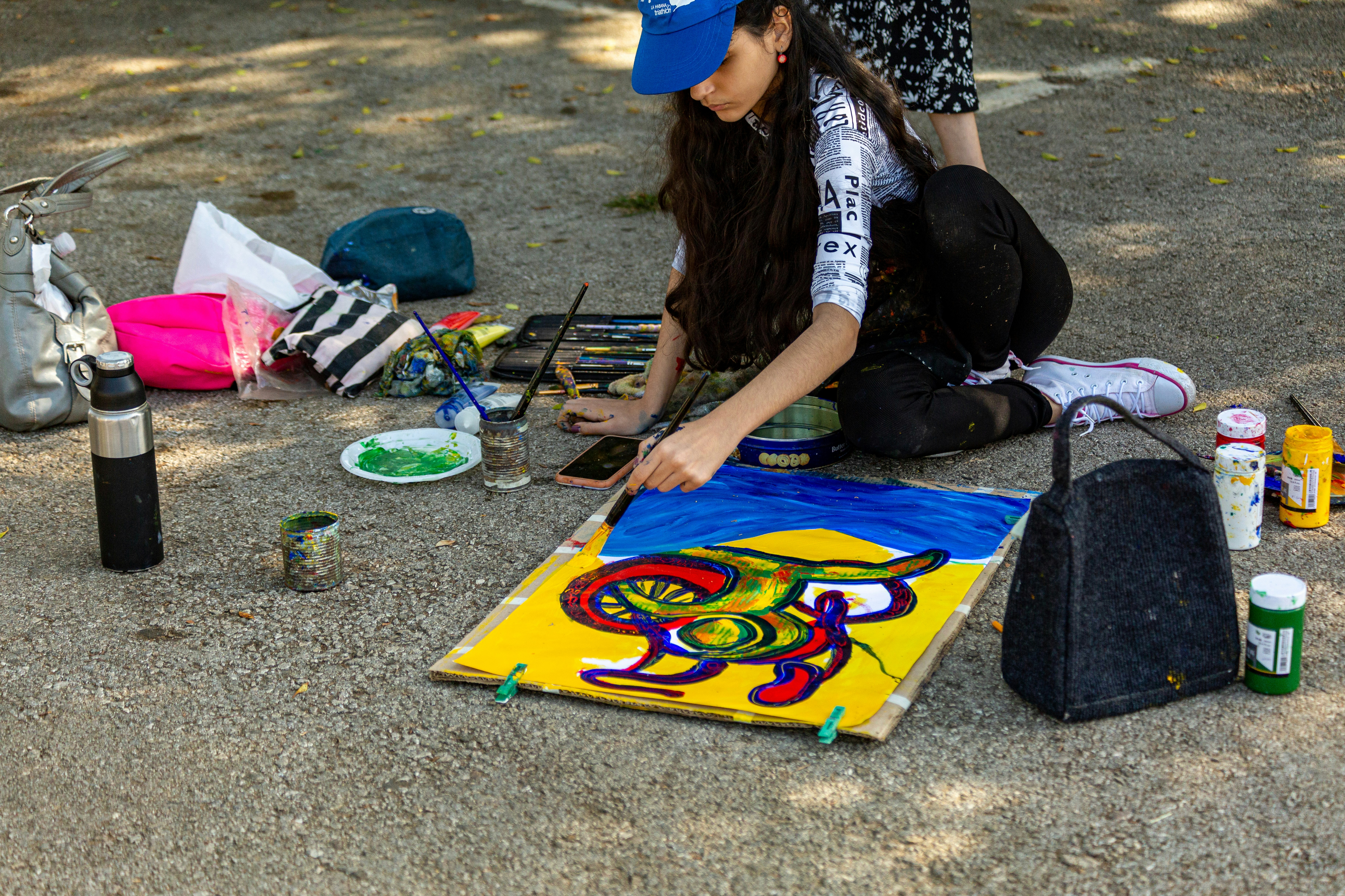 A woman sitting on the ground painting a picture
