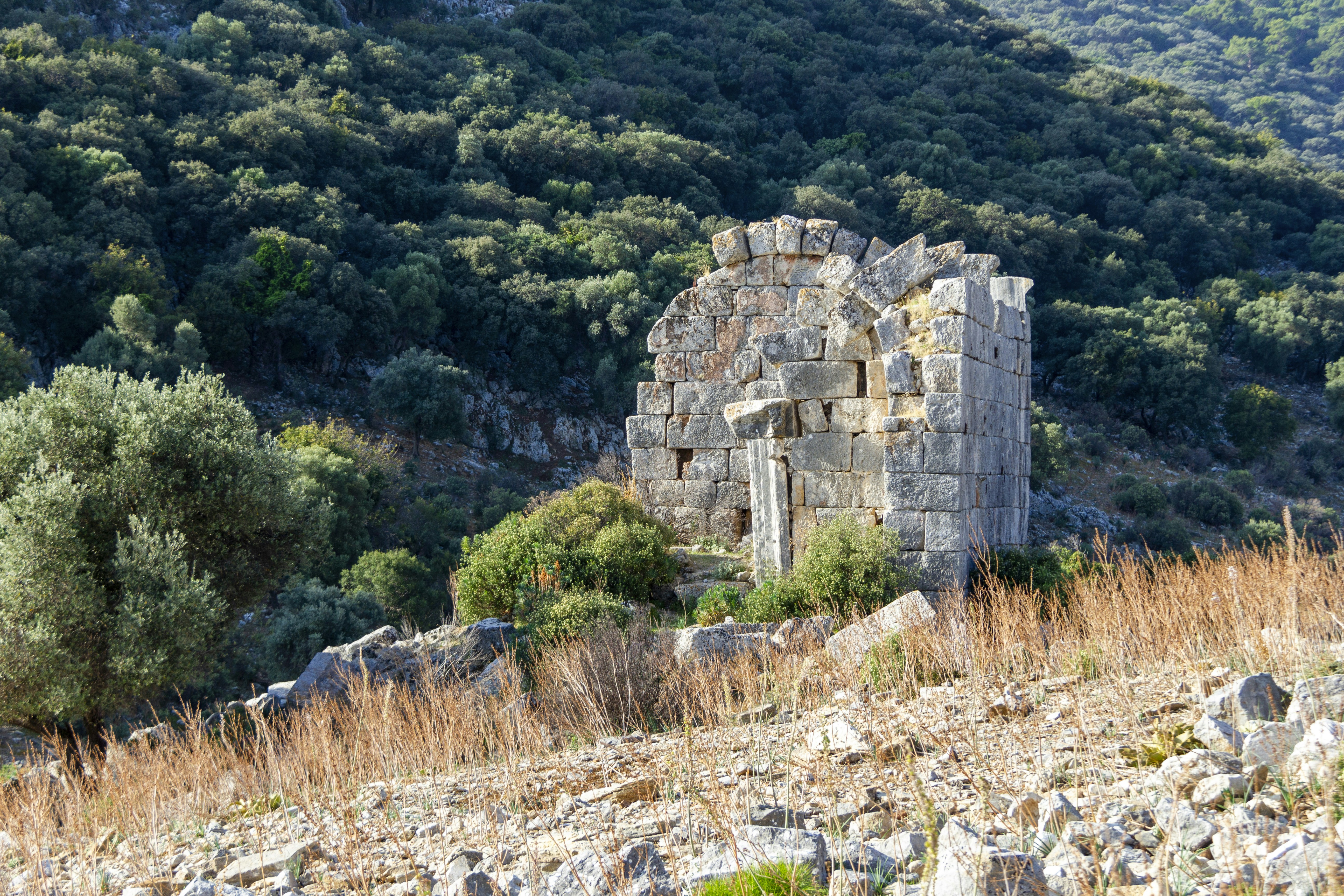 A stone building sitting on top of a lush green hillside, Ancient City Ruins