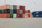 A truck is parked in front of a large stack of shipping containers