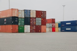 A truck is parked in front of a large stack of shipping containers