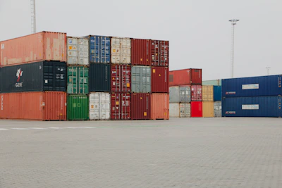 A truck is parked in front of a large stack of shipping containers
