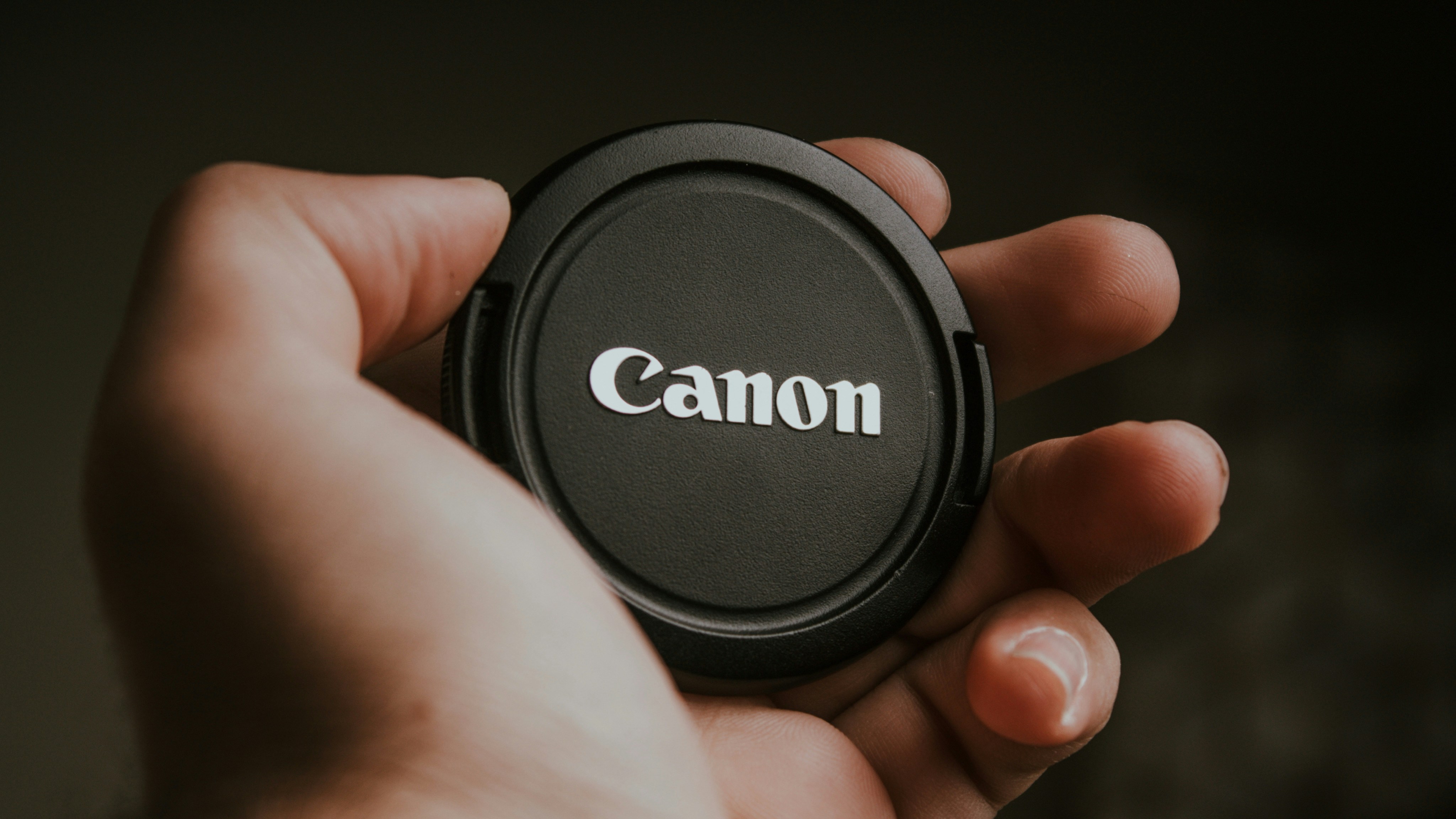 A person holding a camera lens cap in their hand
