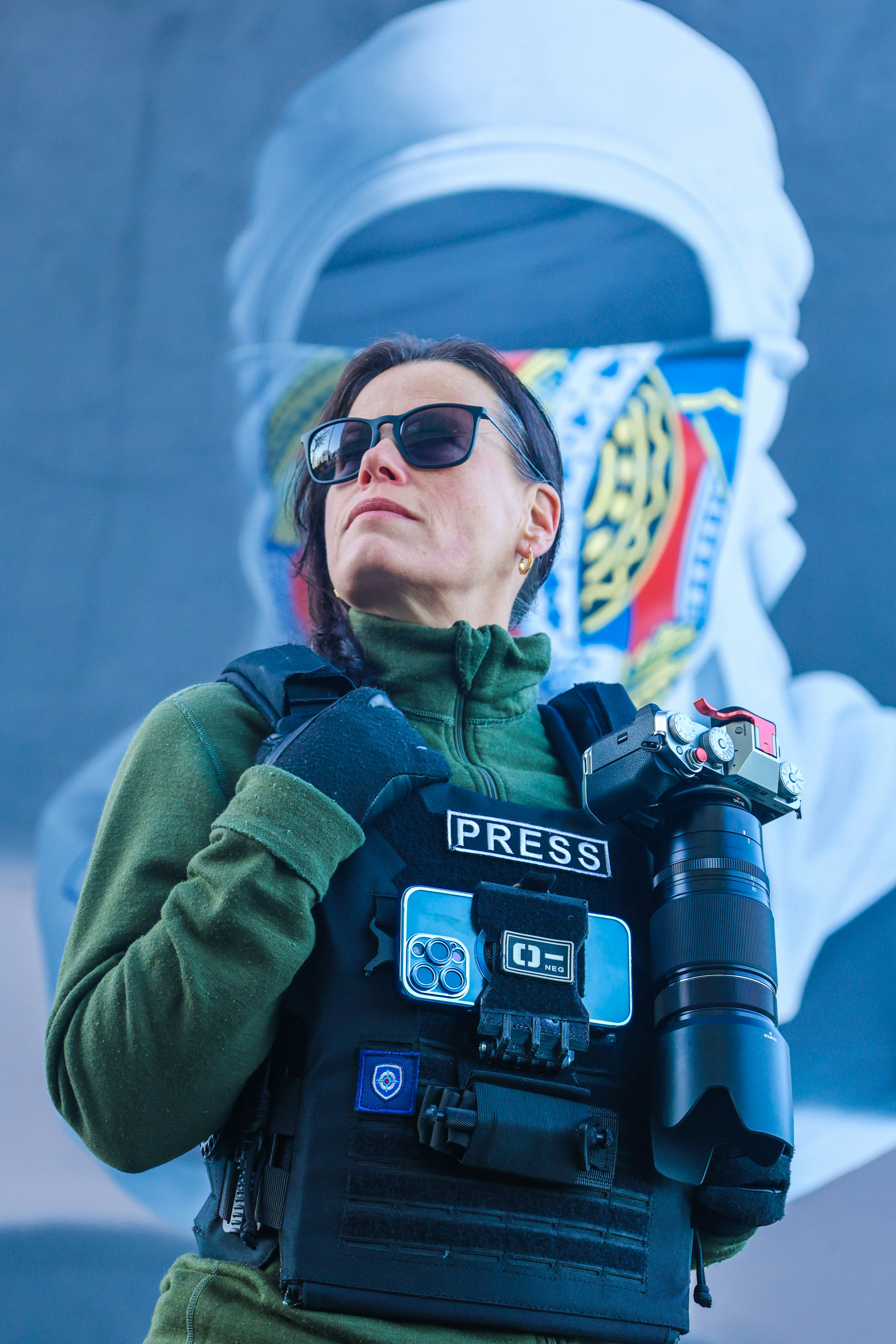 A woman wearing a police vest and holding a camera