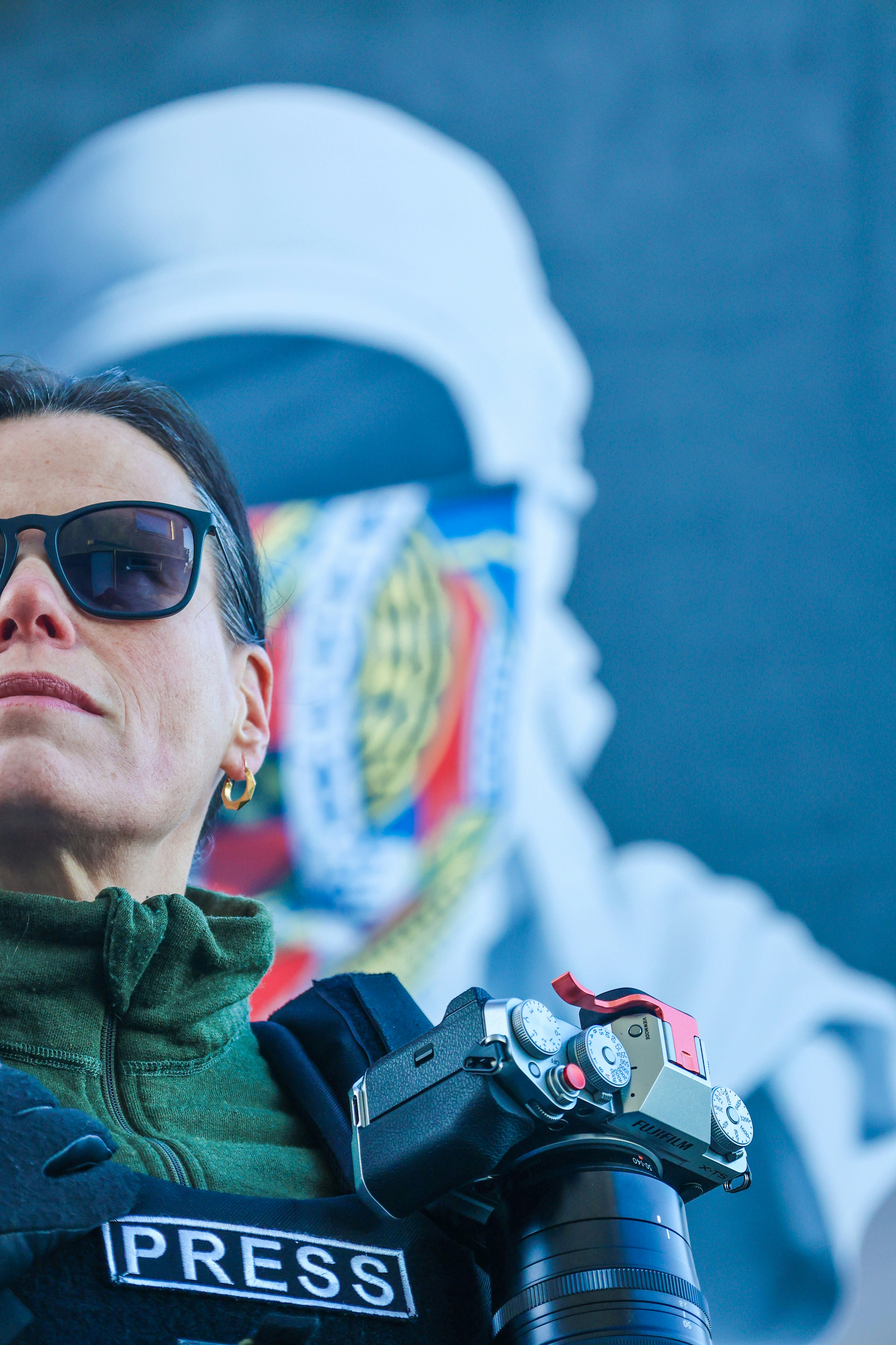 A woman in a green jacket and sunglasses holding a camera