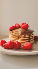A stack of pancakes with raspberries on a plate