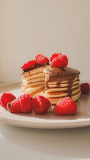 A stack of pancakes with raspberries on a plate