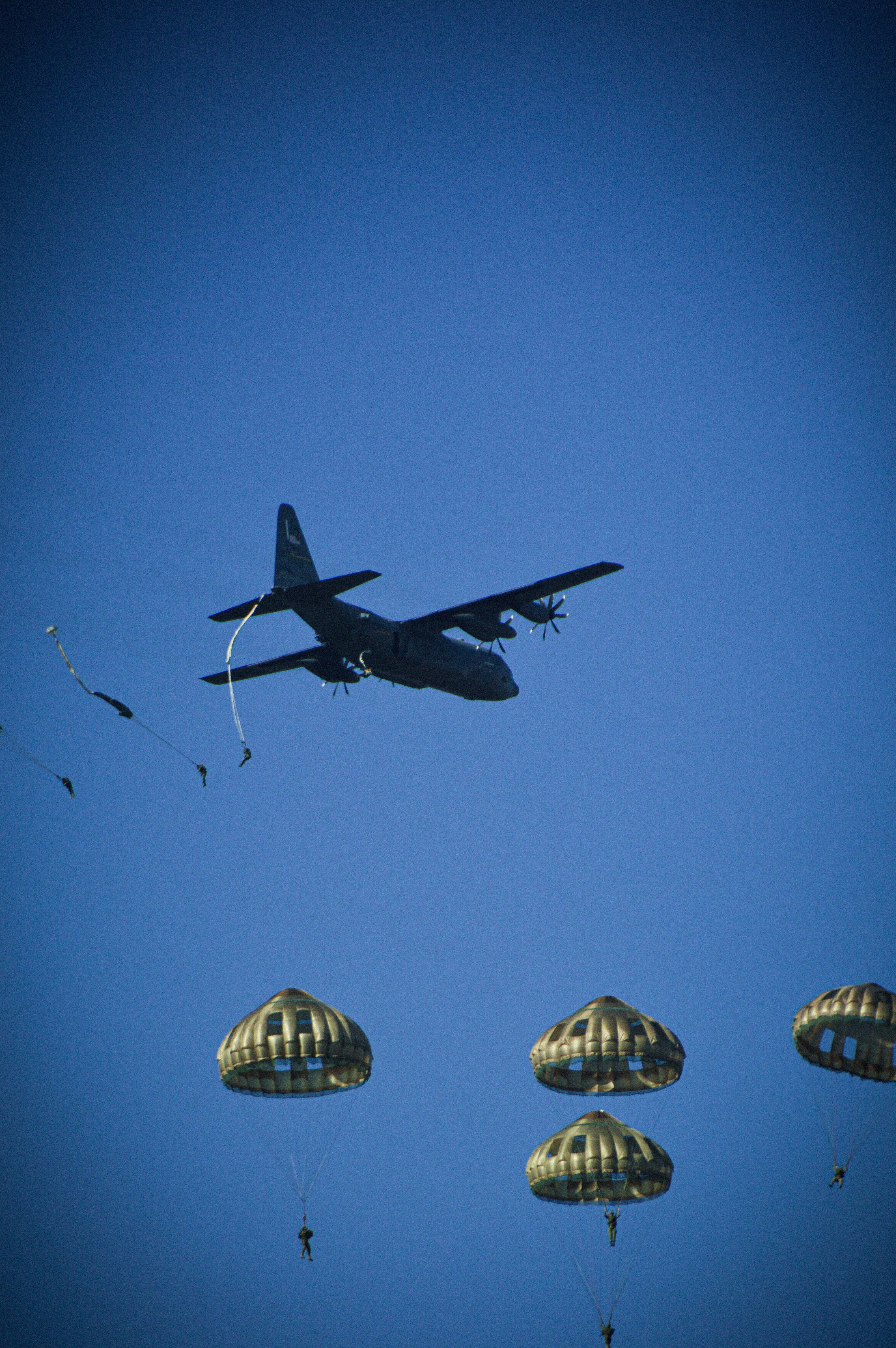 A military transport plane dropping a formation of paratroopers over open sky