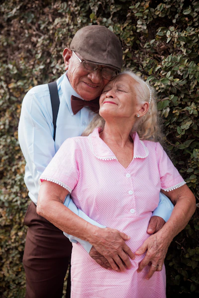 An older couple embracing each other in front of a bush