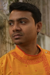 A man in a yellow shirt standing next to a tree
