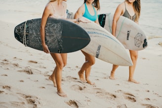 A group of young women carrying surfboards on a beach
